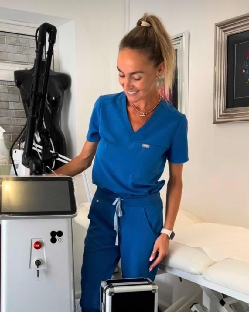 Michelle in her treatment room beside the laser equipment and treatment couch